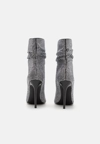 Bottines à talons hauts ornées de strass noirs, présentant un design froncé et une pointe stylisée, avec un talon noir lisse.
