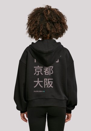 Black oversized hoodie with a front kangaroo pocket, featuring light gray text in multiple languages on the back and a star accent.
