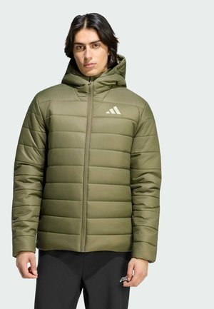 Mann trägt eine olivgrüne Steppjacke mit Kapuze und Reißverschluss sowie einem weißen Logo auf der Brust, kombiniert mit schwarzen Hosen.