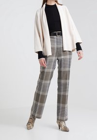 Crème open-front jacket, zwarte ribbed top, grijze checkbroek met blauwe accenten, en slangenprint hoge hakken. Zachte texturen en een getailleerde pasvorm.