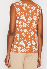 Ärmlös topp i rostorange tyg med vitt blommönster. Rundad halsringning och slät textur, skräddarsydd passform utan synlig hårdvara.