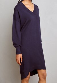 Robe en tricot bleu marine avec un décolleté en V, des manches longues et des accents côtelés. Elle présente un ourlet effilé et une texture douce.