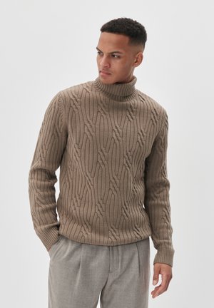 Pulover bej tricotat cu guler înalt, având un model texturat și manșete cu nervuri, combinat cu pantaloni gri deschis. Fundal simplu.