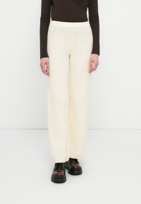 Pantaloni largi cu croială largă, din tricot cu model de cablu, în culoarea crem, cu o textură fină, având o talie înaltă și asortați cu pantofi negri cu platformă groasă.