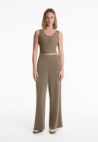 Khaki ribbed crop top with button detail paired with wide-leg, elastic-waist pants in a matching color and soft fabric. Casual look.