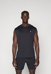 Čierny bezrukávový športový top z ľahkej tkaniny, s jemným logom na hrudi. V kombinácii s čiernymi šortkami.