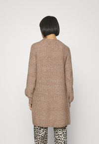 Brun stickad lång cardigan med en avslappnad passform, som har långa ärmar och rund halsringning, i kombination med leopardmönstrade byxor.