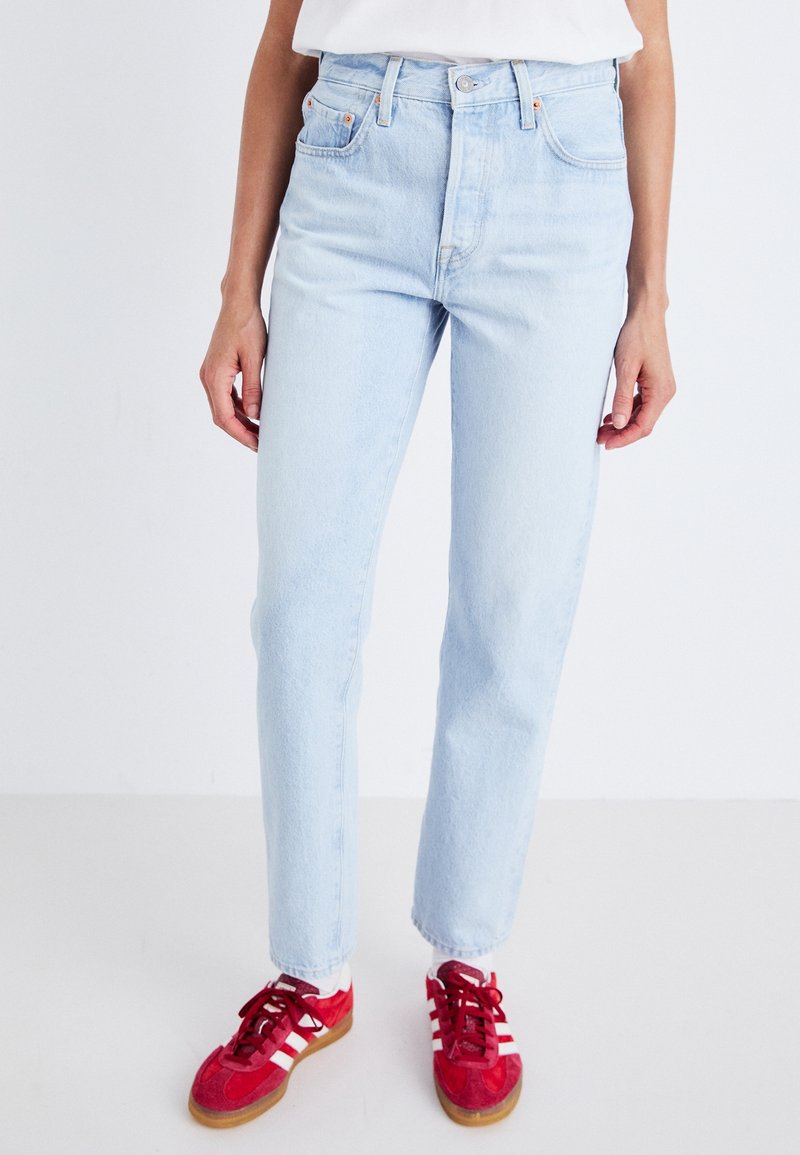 Jeans de tiro alto en azul claro con pernera recta, diseño clásico de cinco bolsillos y una sutil textura desgastada. Acentuados con costuras en naranja.
