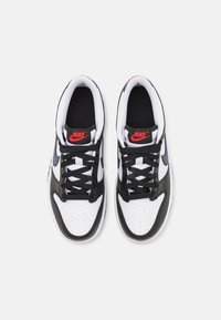 Juodos ir baltos sportinės bateliai su lygaus odos viršumi, perforuotu pirštu, juodomis raištelėmis ir raudonu Nike logotipu ant liežuvio.