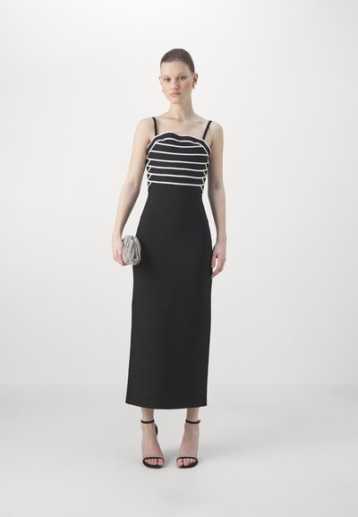 Abito nero con strisce orizzontali bianche nella parte superiore, corpetto aderente e un lungo design a coste. Abbinato a una pochette argentata texture.