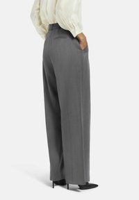 Pantalons gris à jambes larges en tissu texturé, dotés d'une taille, de poches latérales et d'une silhouette ajustée. Associés à des talons noirs.