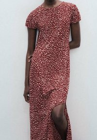 Robe rouge avec un motif à taches blanches, manches courtes et fente sur le côté. Fabriquée en tissu léger, elle présente une coupe décontractée et un col rond.