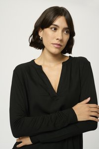 Top lung cu maneci lungi, de culoare neagră, cu decolteu în V, realizat dintr-un material moale. Se remarcă printr-o croială lejeră și detalii subtile de cusătură.