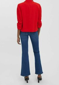 Punainen bleiseri käännetyillä hihoilla, yhdistettynä sinisiin liehuviin farkkuihin. Bleiserissä on jämäkkä muotoilu, ja farkuissa on koristeompeleita.