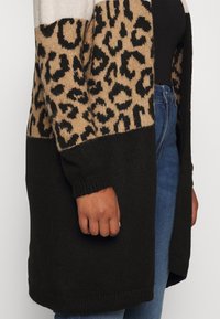 Dlouhý cardigan s leopardím potiskem v béžové a černé barvě, s pevným černým spodním dílem. Pletená textura a žebrované manžety.