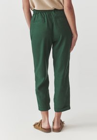 Pantalon en lin vert au fit décontracté, avec une taille élastique et des ourlets retroussés, comportant deux poches arrière. Le matériau semble doux et texturé.
