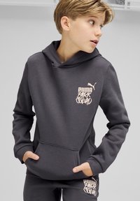Sudadera gris oscuro con bolsillo tipo canguro, puños acanalados y un gráfico de logotipo en rosa que dice "PUMA PARK SQUAD" en la parte frontal.