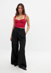 Červený čipkovaný crop top s kvetinovým motívom a nastaviteľnými ramienkami, doplnený o čierne voľné nohavice s vysokým pásom a čierne špicaté topánky.