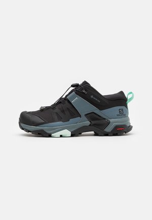 Chaussure de trail running dotée d'une tige en mesh noir avec des accents turquoise, d'une semelle en caoutchouc durable et d'un système de laçage rapide pour un ajustement sécurisé.