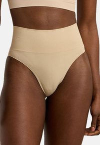 Högmidjade beige underkläder tillverkade av ett slätt, elastiskt material med en sömlös design och inga synliga sömmar eller hårdvarudetaljer.