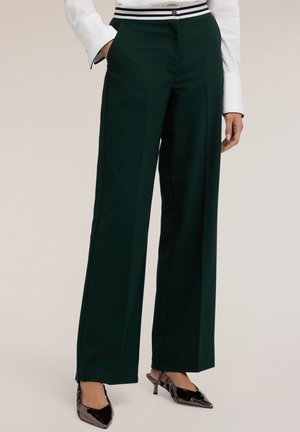 Pantaloni larghi verdi realizzati in un tessuto liscio con una cintura a righe bianche e nere. Presentano tasche laterali e un design sartoriale.