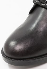 Mustat nahkakengät, pyöreä kärki, sileä pinta hienovaraisella kiillolla, varustettuna mustilla nauhoilla ja kestävästä mustasta kumipohjasta.