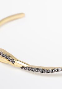 Bracciale placcato in oro con design curvo, caratterizzato da una linea di piccoli accenti scintillanti e una superficie liscia e lucida.