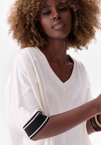 White V-neck top with relaxed fit, features black and white striped accents on sleeves, smooth texture, and soft material.