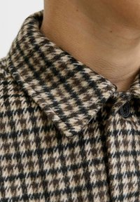 Camicia con colletto in lana a quadri marroni e beige, caratterizzata da un colletto robusto, un tessuto texturizzato e dettagli con bottoni neri.