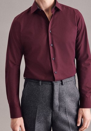 Camicia bordeaux a maniche lunghe con taglio aderente, caratterizzata da bottoni blu e colletto a fantasia, abbinata a pantaloni tailored in lana grigia.