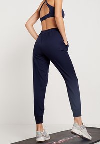 Marineblauwe sportbroek met een taps toelopende pasvorm, elastische tailleband en zijzakken, gemaakt van een gladde, lichtgewicht stof.