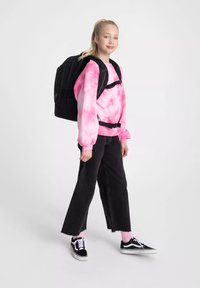 Zaino nero, felpa rosa tie-dye, jeans neri a gamba larga, calzini rosa, scarpe nere e bianche. Tessuti morbidi, vestibilità casual.