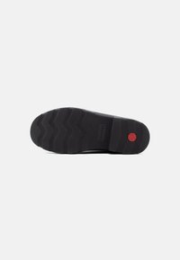 Black rubber shoe sole with a zigzag tread pattern and a red circular accent. Notable texture is pebbled for grip.