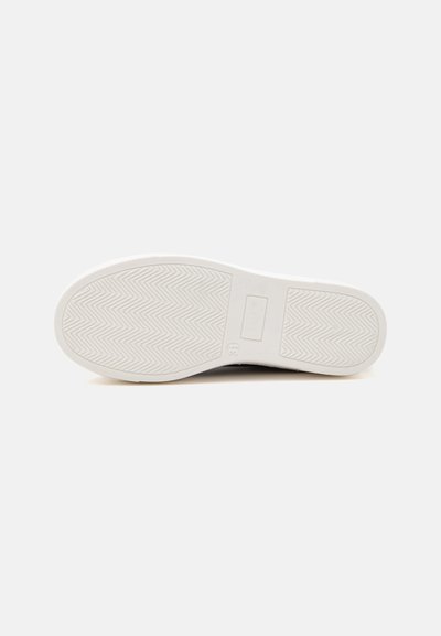 Semelle de chaussure blanche avec motif en chevrons et une section rectangulaire près du talon, présentée sur un fond clair uni.