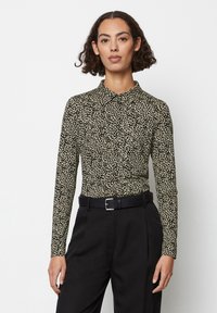 Camicia a maniche lunghe nera con motivo astratto beige, dotata di colletto e design aderente. Abbinata a pantaloni neri e una cintura.