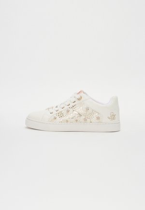 Hvid lavtop sneakers med blomsterudskæringsmønstre, gyldne accenter og snørebånd mod en enkel lys baggrund.