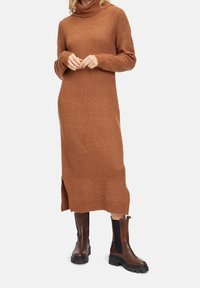 Lång, ribbad, brun stickad klänning med hög polokrage och sidofickor. Bärs med mörkbruna ankelstövlar med elastiska paneler.