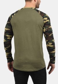 Langsleeve shirt met een olijfgroene body en camouflagepatroon mouwen in tinten groen, bruin en beige. Ronde hals.