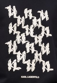 Čierna látka s opakovaným bielym grafickým vzorom písmen "K" a "L". Obsahuje text značky: "KARL LAGERFELD" pod ním.