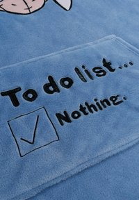 Coperta morbida blu con testo ricamato in nero: "Lista delle cose da fare… Niente." Include una casella di controllo con una spunta.