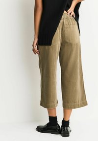 Olive green corduroy culottes with wide legs and a textured surface. Features elastic waistband and two back pockets. Worn with black shoes.