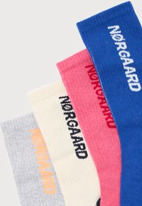 Τέσσερις ριγωτές κάλτσες σε γκρι, εκρού, ροζ και μπλε, κάθε μία με το κείμενο "NORGARD" σε αντίθετα χρώματα κατά μήκος της μανσέτας.