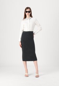 Witte langslavende shirt met een versierde kraag, gecombineerd met een donkergrijze ribgebreide midi-rok en beige hakken sandalen.