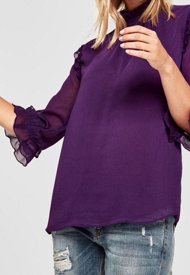 Blusa viola con maniche trasparenti e arricciate, dal morbido tessuto. Presenta una vestibilità comoda e tessuti sovrapposti, abbinata a jeans strappati.