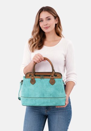 Young woman in white top and jeans holding a large turquoise and brown leather handbag with double handles and zipper closure.