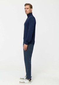 Kék garbó pulóver testhezálló fazonnal, szürke laza szabású nadrággal és fehér sportcipővel, szürke részletekkel kiegészítve.