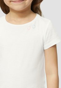 Weißes Baumwoll-T-Shirt mit rundem Halsausschnitt, kurzen Ärmeln und gestickten rosa und blauen Herzakzenten auf der linken Schulter.