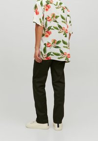 Camisa de manga corta con fondo blanco y patrón floral melocotón, combinada con pantalones oscuros y zapatillas blancas.