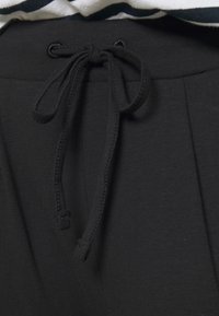 Gros plan sur un cordon de serrage noir noué en nœud sur la ceinture élastique d'un pantalon en tissu noir.