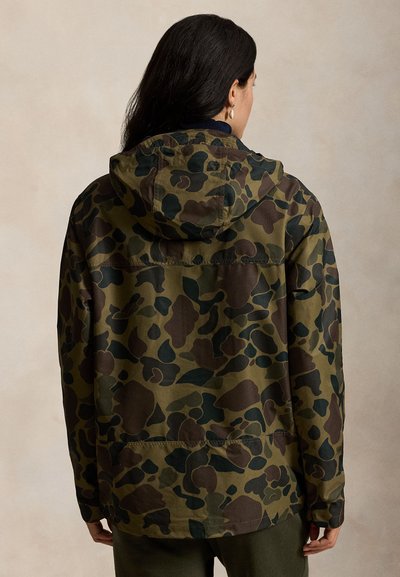 Casaco camuflado apresenta uma mistura de padrões em verde escuro e castanho, com capuz e mangas compridas, confeccionado em material leve.